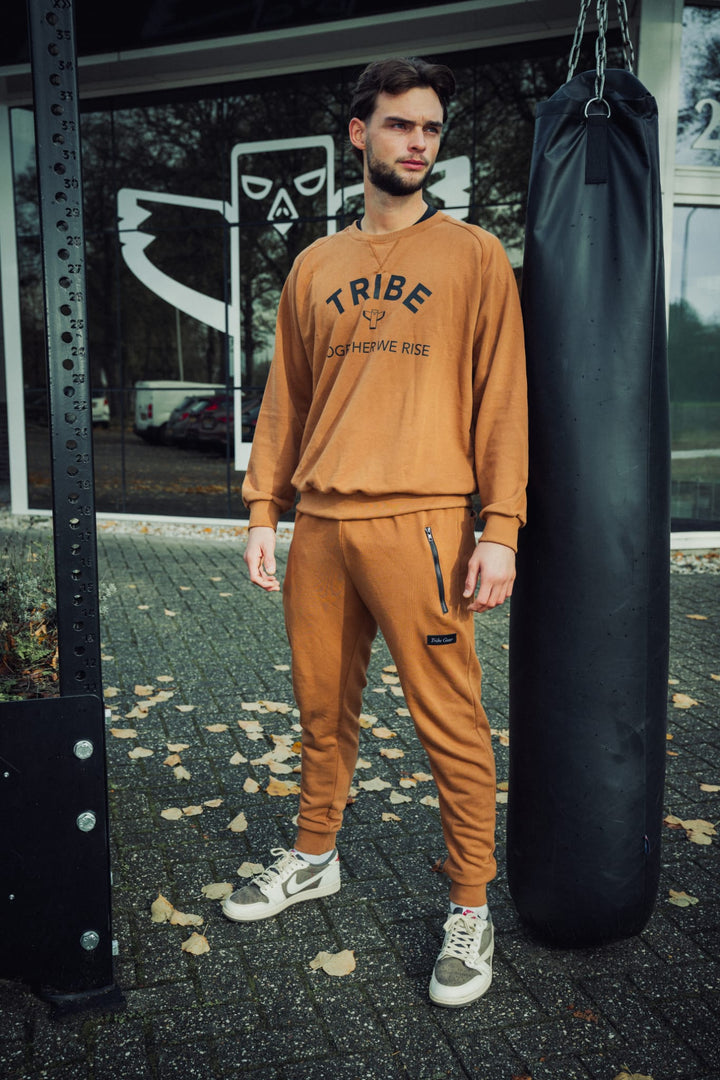 Sporter draagt bruin TribeGear trainingspak bij bokszak voor kickboks training